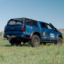 Blue Ford truck with a bed rack in a grassy field
