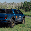 Blue truck with 'Mick Tighe Outdoors' branding parked on a grassy area with trees in the background.